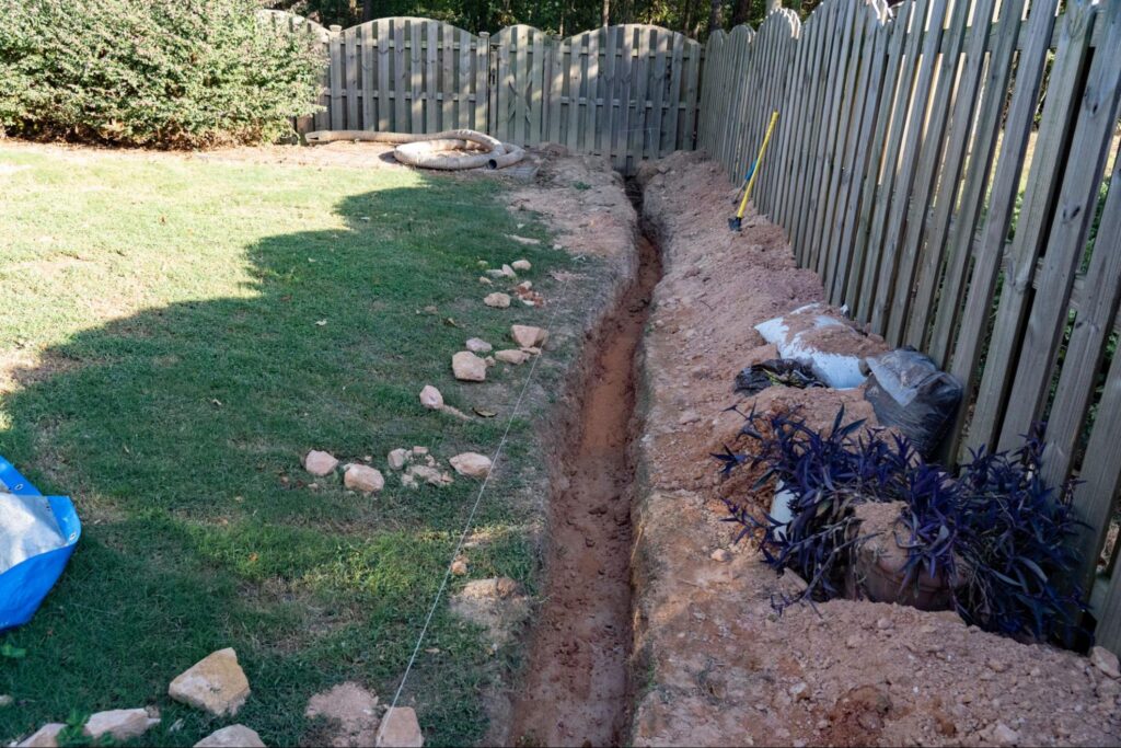 Preparing for French drain pipe to be laid for subsurface water drainage.