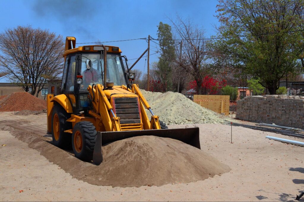 Backhoe loader grading and moving fill dirt during a site preparation project in Boise, ID.