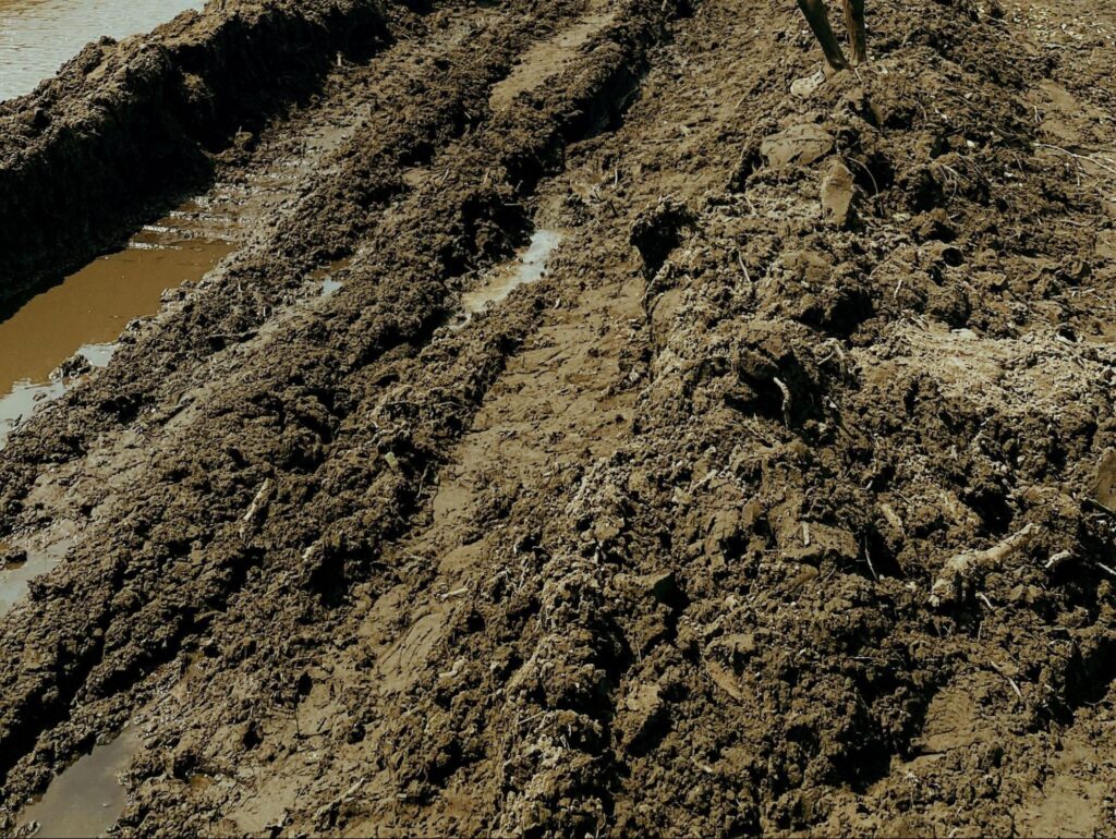 A freshly dug drainage trench holding standing water beside saturated soil during yard drainage work in Boise, ID.