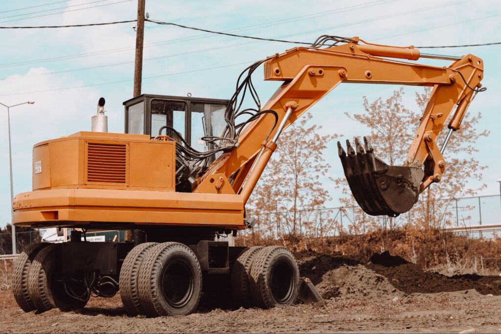 Wheeled excavator with bucket raised over freshly dug soil, ready for septic excavation