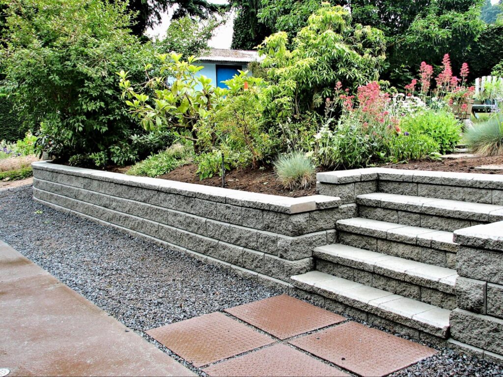 A segmental block retaining wall with capstones and built-in steps holds a raised garden bed, a common style for retaining wall installation in Boise.