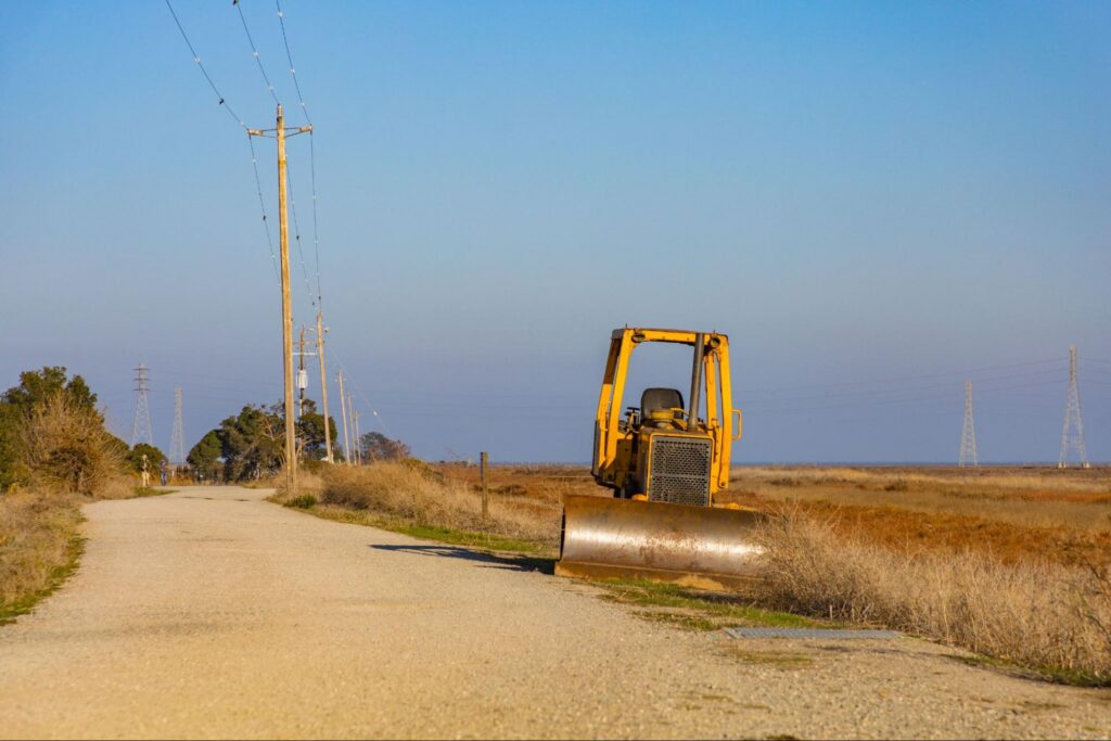 A compact bulldozer parked beside a gravel path in an open field.